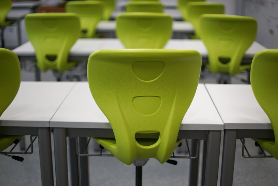 An empty modern classroom featuring rows of vibrant green plastic chairs and white desks