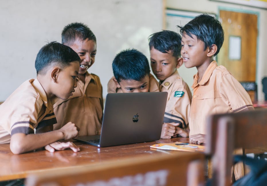 A group of young boys in school uniforms collaborating over a laptop in a classroom setting